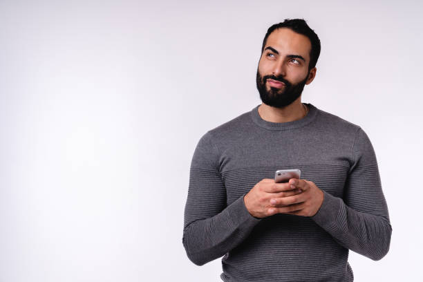 istock Dreamy young Middle Eastern man using smartphone in casual attire isolated over white background 1298353605