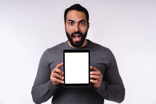 istock Shocked young handsome Middle Eastern man with blank tablet in casual attire isolated over white background 1298353669