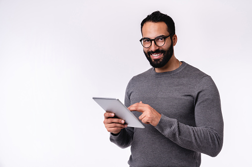 Side view photo of young handsome arab man using tablet in casual outfit isolated over white background