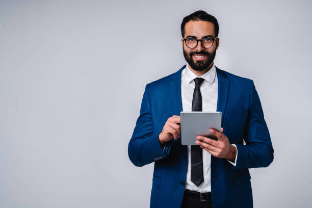 istock Happy successful 25s Arab businessman in office outfit using tablet isolated over grey background 1298354219