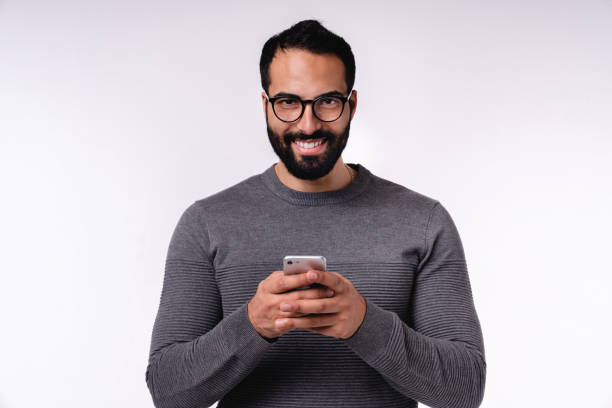 istock Smiling confident 25s Arabian man in casual outfit using mobile phone isolated over white background 1298354381