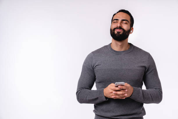 istock Dreamy young attractive Middle Eastern man using smart phone in casual clothing isolated over white background 1298354382