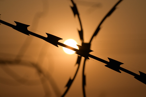 Sunset behind a strong steel fence guarding the border.