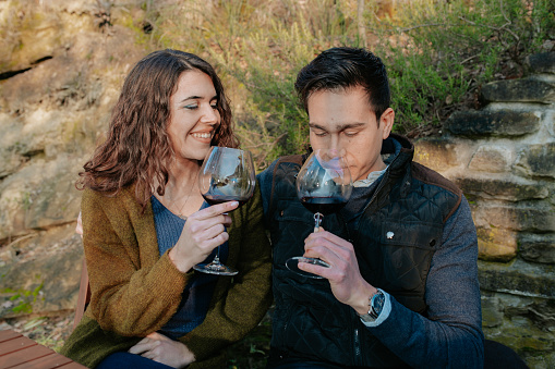Young romantic couple sitting in a garden tasting a glass of red wine during a picnic.
