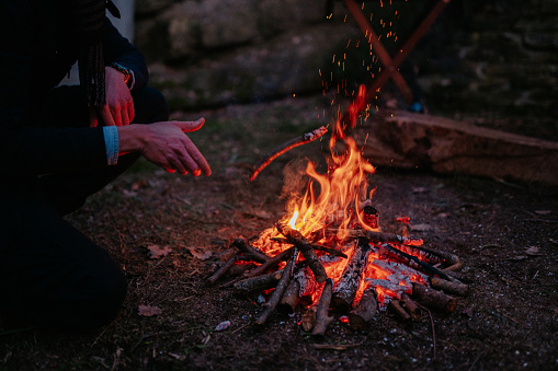 Unrecognizable man throwing wood on fire. Camping, wildlife concept.