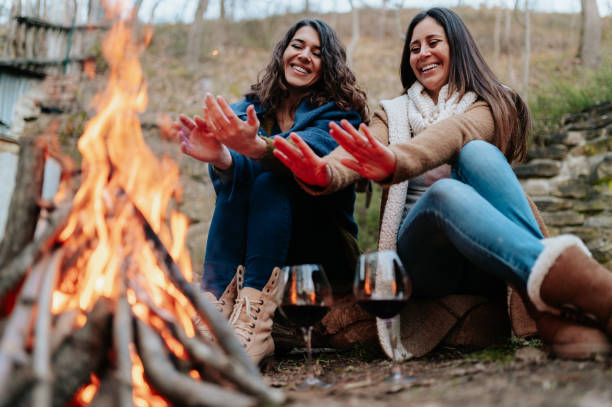 mujeres sonrientes calentando junto al fuego. copas de vino tinto - fire pit fire camping burning fotografías e imágenes de stock