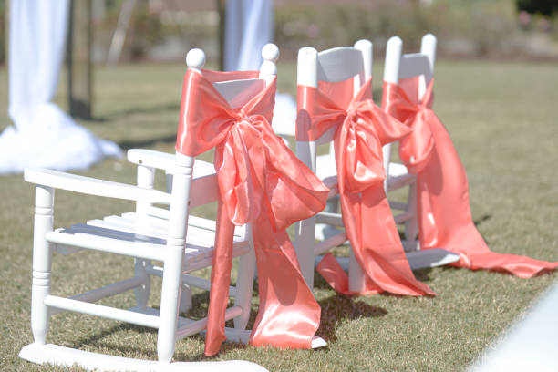 istock Three white  rocking chairs with pink lace bows and sashes on green lawn 1298360721