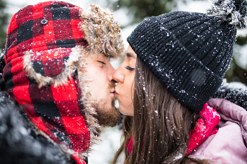 An attractive young couple is kissing out on a snowy day