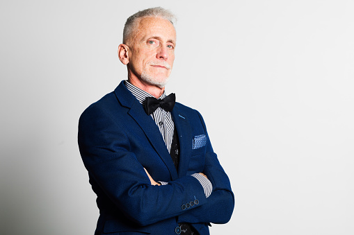 Senior man dressed in suit and bowtie arms crossed with a stern expression studio portrait.