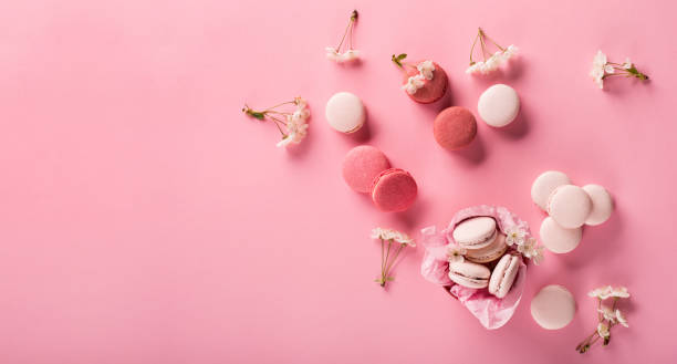 istock Rose macaroons in gift box and Cherry blossoms. Sweet macarons present on pink background. 1298368061