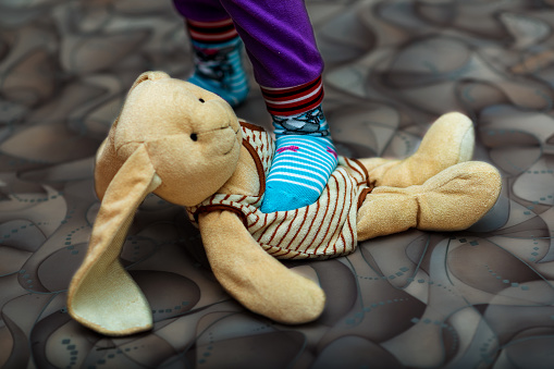 A small child stepping on a stuffed rabbit - the concept of domestic violence. Selective Focus