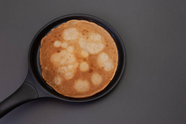 A delicious looking pancake cooking in a pan on a gray background