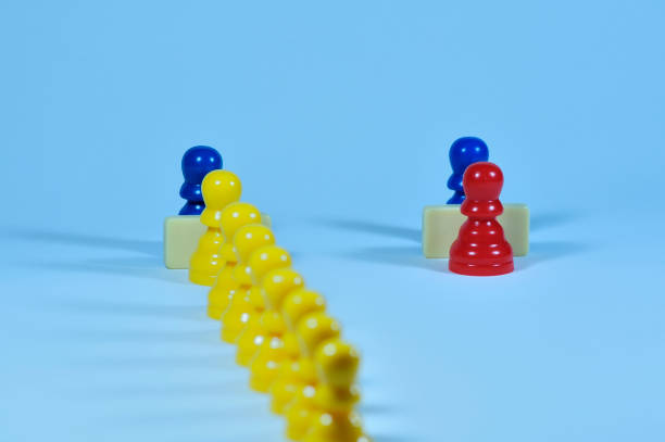 istock Concept with colored pawns. Privileges. An individual figure is served at one counter while many others wait their turn at another counter. 1298373079
