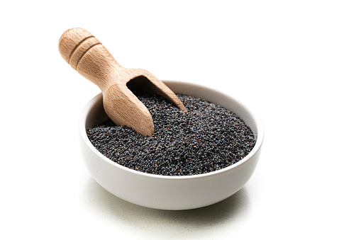 Poppy seeds in a white bowl isolated on white background. A wooden serving scoop is inside the bow. High resolution 42Mp studio digital capture taken with Sony A7rII and Sony FE 90mm f2.8 macro G OSS lens