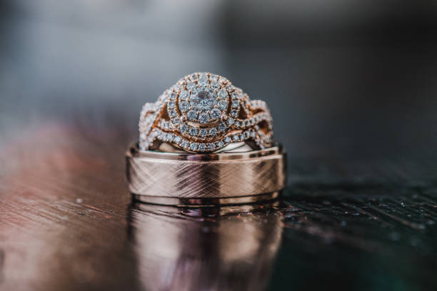 istock Ornate gold wedding rings with many diamonds in circular pattern on reflective wood surface 1298377559