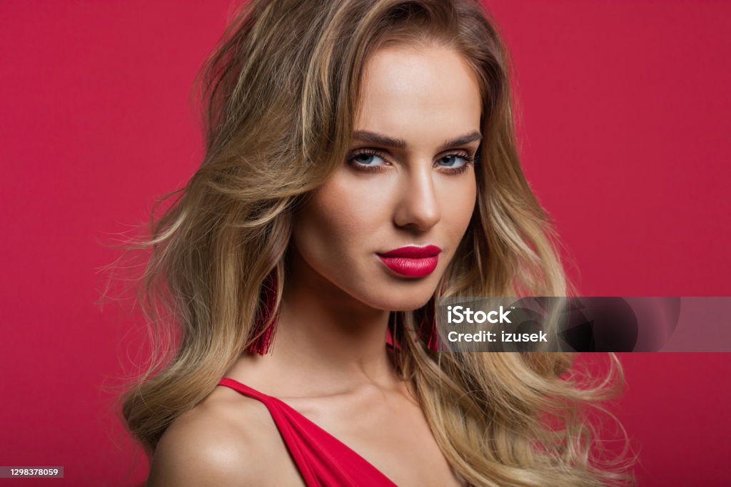 Portrait of beautiful woman on red background Headshot of sensual long blond hair woman wearing red dress, looking at camera. Close up of face. Studio shot against red background. 20-29 Years Stock Photo