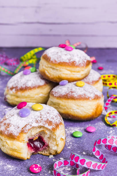 krapfen, berliner ou beignets avec banderoles, confettis et fèves au chocolat. image colorée de carnaval ou d’anniversaire sur le fond pourpré, verticale avec l’espace de copie. - fasching photos et images de collection