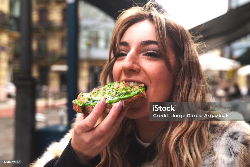 Young caucasian woman having breakfast at a terrace eating an avocado toast. Eating Stock Photo