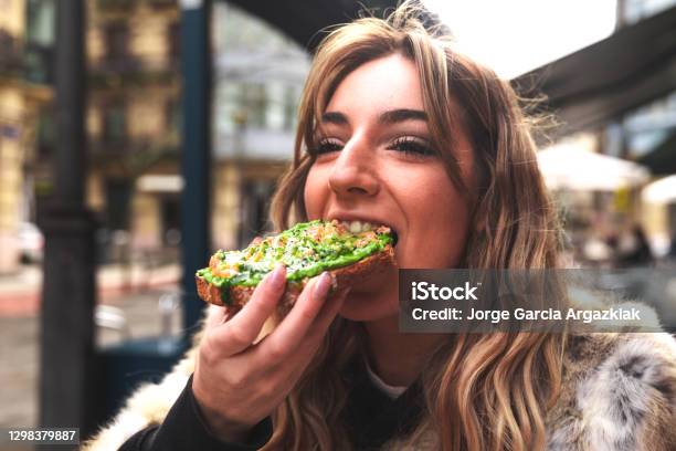 Young Caucasian Woman Having Breakfast At A Terrace Eating An Avocado Toast Stock Photo - Download Image Now