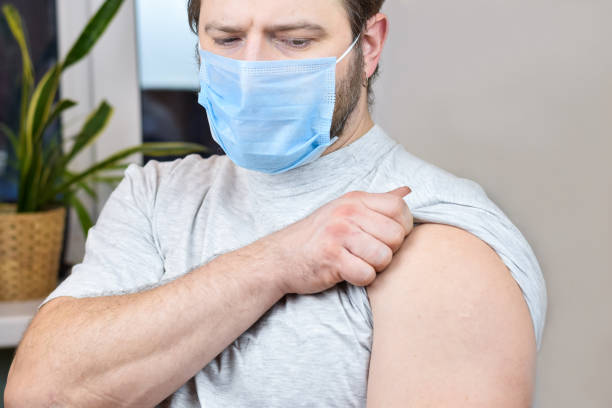 青い保護マスクを着用したひげを生やした男が予防接種を受ける準備をしている。covid-19ワクチン接種キャンペーン。 - roll of arms ストックフォトと画像