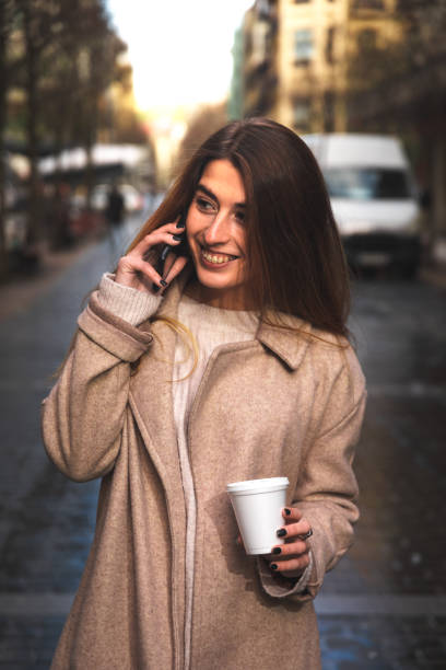 istock Young caucasian woman talking by phone while drinking a coffee in a plastic cup at Donostia-San Sebastian downtown; Basque Country. 1298380020