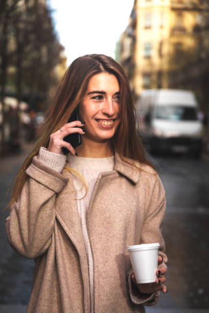 istock Young caucasian woman talking by phone while drinking a coffee in a plastic cup at Donostia-San Sebastian downtown; Basque Country. 1298380220