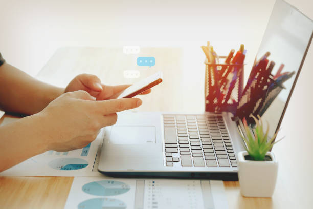istock Business man hand using and touching on mobile smart phone, chatting via smartphone application and working on laptop computer 1298383114