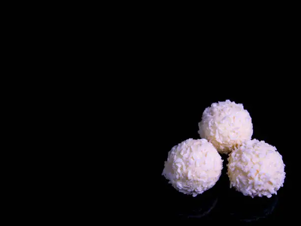 Photo of Round white candy with coconut flakes on a black background.