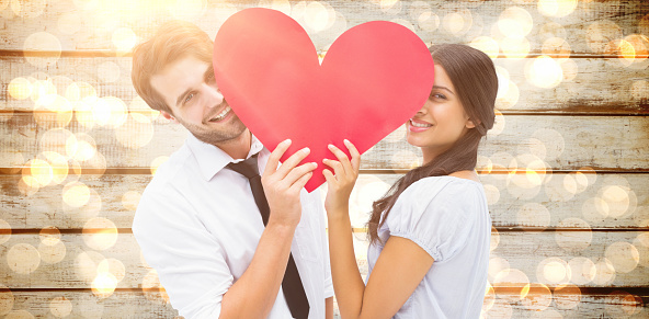 Couple smiling at camera holding a heart against blurred yellow light