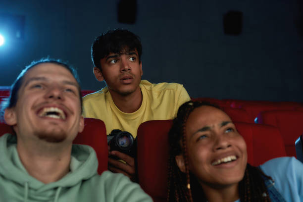 istock Young guy looking scared, using his video camera while recording a pirated movie at the cinema 1298390052