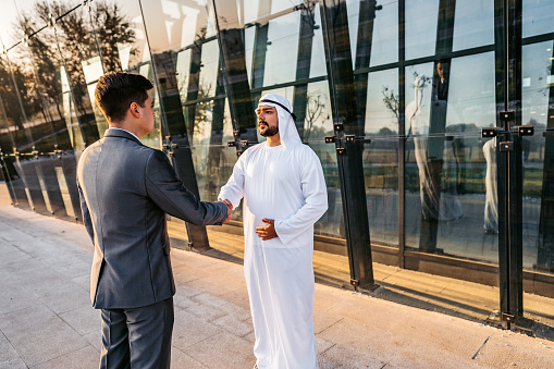 Emirati executive man and a western businessman making agreement and shaking hands.