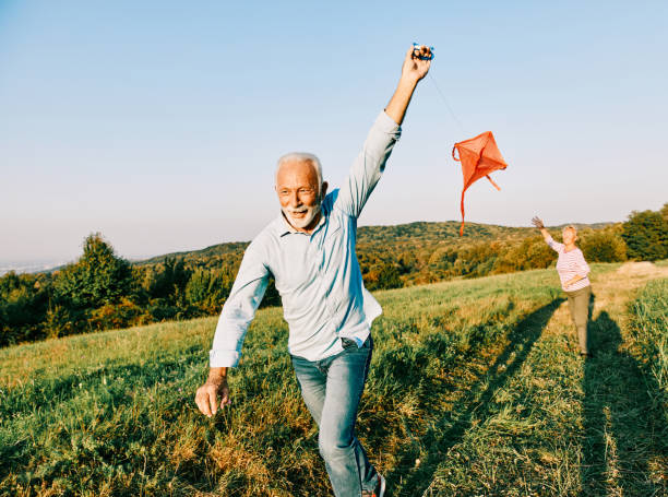 woman man outdoor senior couple happy lifestyle retirement together smiling love kite run nature mature Happy active senior couple with kite outdoors motion stock pictures, royalty-free photos & images