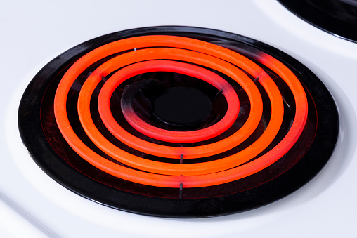 Horizontal shot of a single hot burner on top of a white stove top.