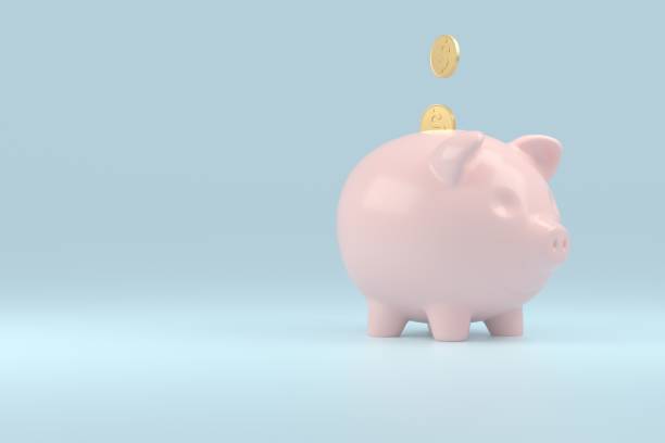 istock Pink piggy bank sideways with falling coins a blue background with empty space for the text. Concept of saving money 1298395786
