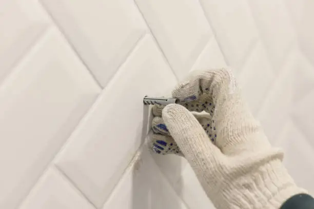 Worker's hand in glove inserts wall pvc dowel in wall cladded with tile ceramic.