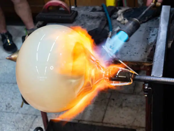 Manual glassblowing process.  Man Working on a big glass art object on pipe with gas torch blue flame