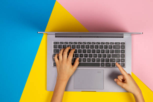 istock Kid hands typing on laptop computer keyboard on multicolored background, top view 1298406847