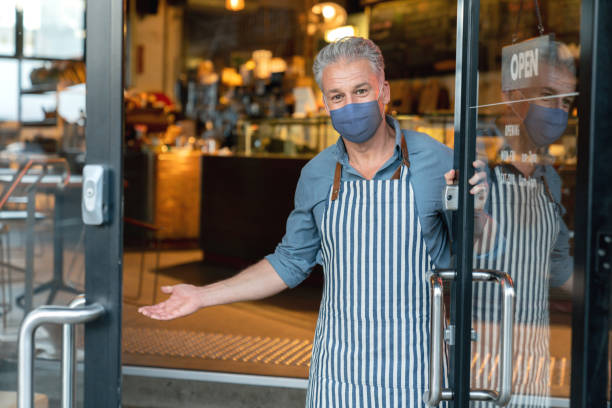 istock Business owner wearing a facemask while welcoming customers to his cafe 1298407408