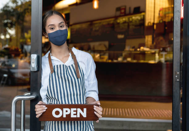 istock Waitress wearing a facemask at a cafe and holding an open sign while waiting for clients 1298407410