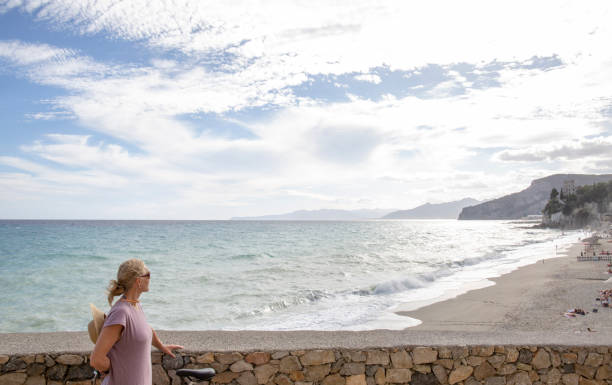 istock Woman with bicycle looks over beach and coastline 1298410810
