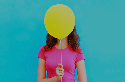 Woman covering her head with yellow balloon on colorful blue background
