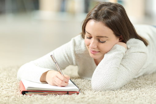 Happy teen writing notes on notebook at home