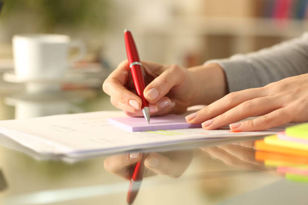 istock Woman hand writing on sticky note on a table at home 1298413392