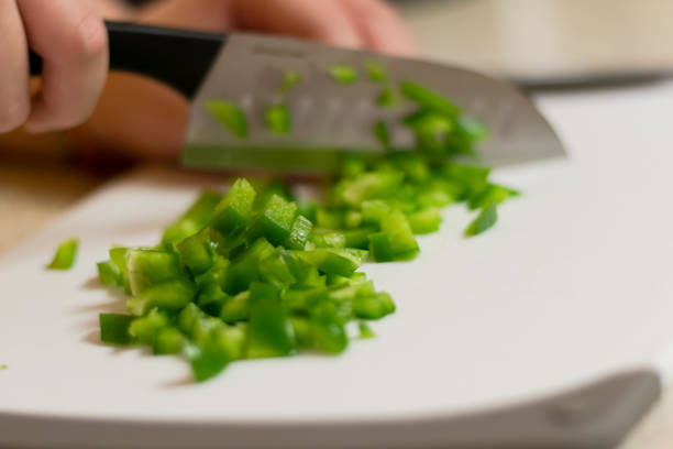 A fresh green bell pepper being chopped in to diced pieces on a white cutting board with a knife. A home chef cutting up vegetables to use in a recipe. green bell pepper stock pictures, royalty-free photos & images