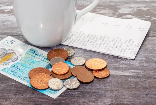A shopping receipt with some coins and a five pound note and a cup