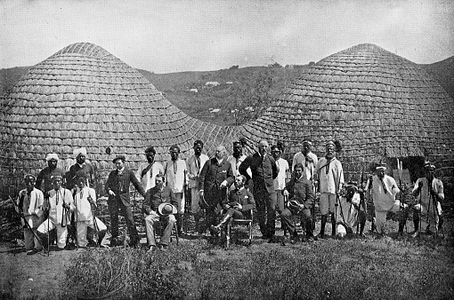Group of Boer men and AmaZulu chiefs Zulu kraal (village) in the Kingdom of Zululand, South Africa. Vintage photo etching circa 19th century. It was absorbed into the British Colony of Natal in 1897, and then the Union of South Africa in 1910.