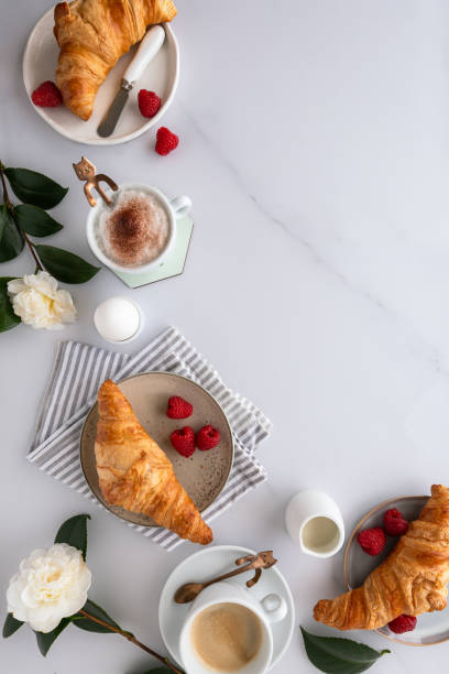 istock Flat lay of a breakfast table with croissants, coffee, fruit and flowers on a white marble surface 1298416918