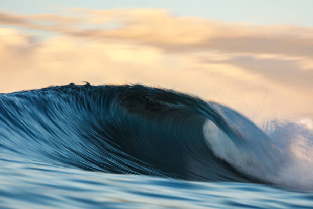 istock Cresting wave breaking in the ocean against a soft peach pastel sky 1298417476
