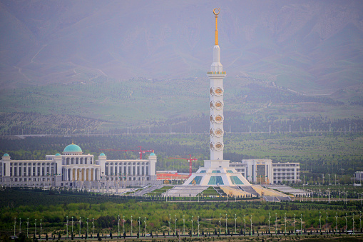Ashgabat, Turkmenistan: Constitution monument and government buildings on Archabil avenue with mountains in the background - marble clad column with gilded traditional ornaments, topped by a crescent with stars- Türkmenistanyň Konstitusiýa binasy.