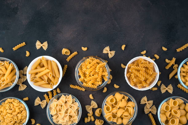 Bowls of pasta of different varieties on a dark concrete background Bowls of pasta of different varieties on a dark concrete background. Top view, with space to copy. Concept of products, culinary backgrounds. carbohydrate food type photos stock pictures, royalty-free photos & images